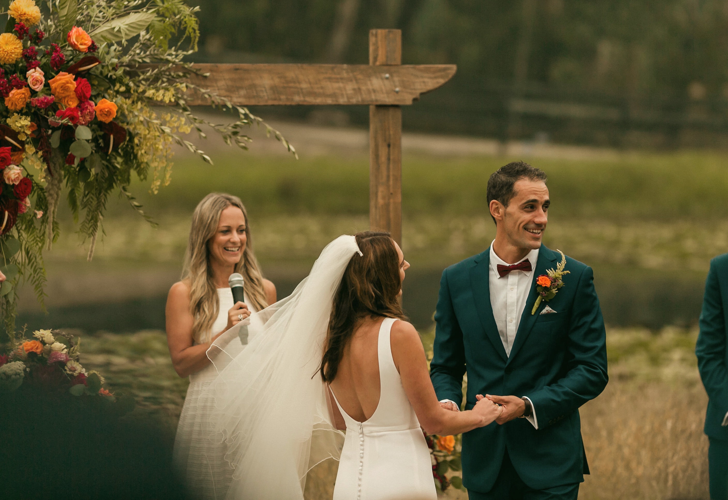 A couple surrounded by guests at a beachside ceremony, mid-laugh during their vows